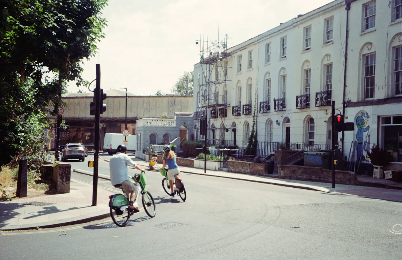 Two people cycling hire bikes past white terraced houses