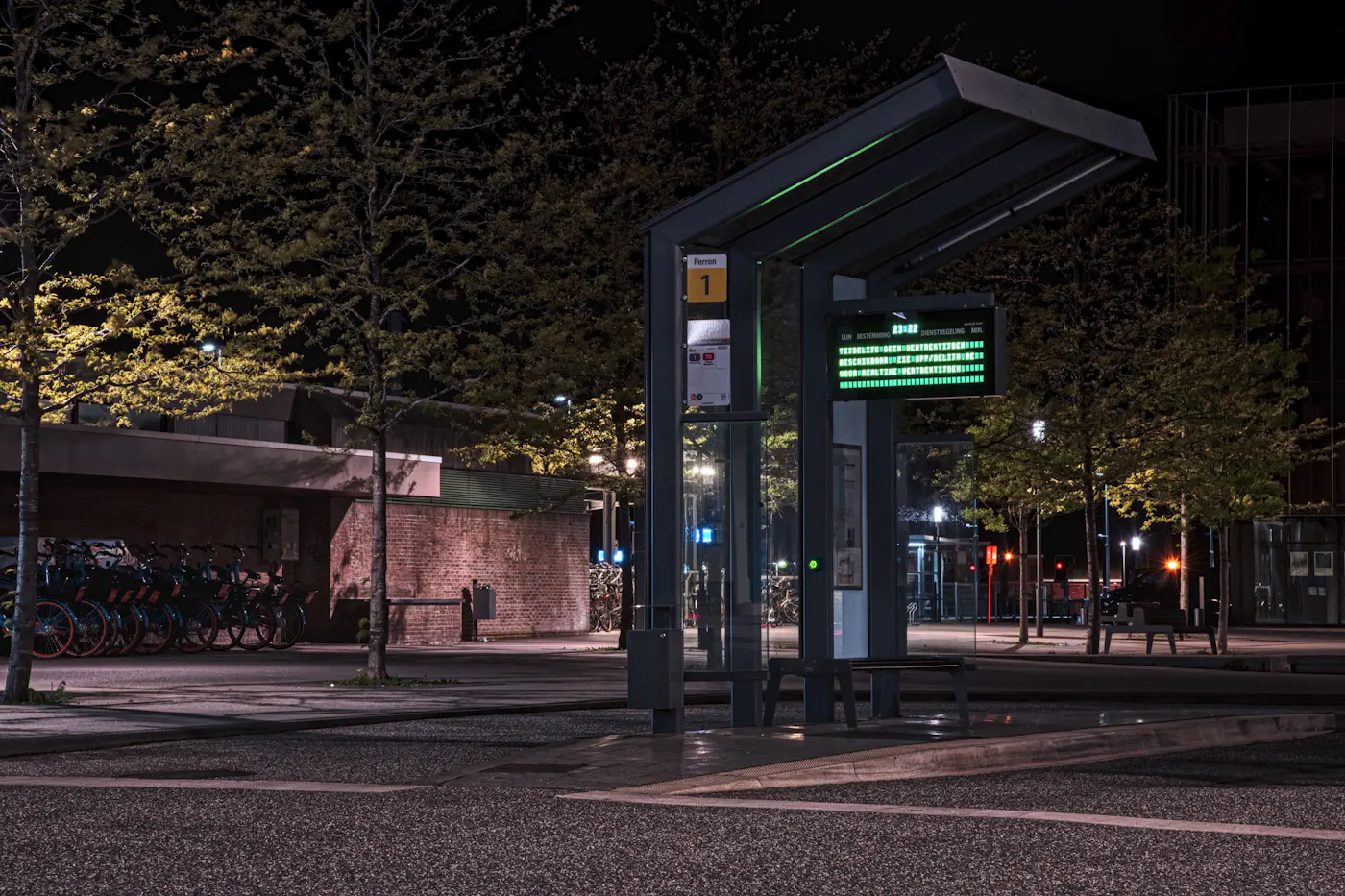 A bus shelter with a live departures board, lit up at night